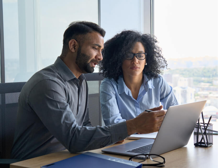 Two business professionals analyzing data on a laptop, discussing labor supply and demand trends in the job market.