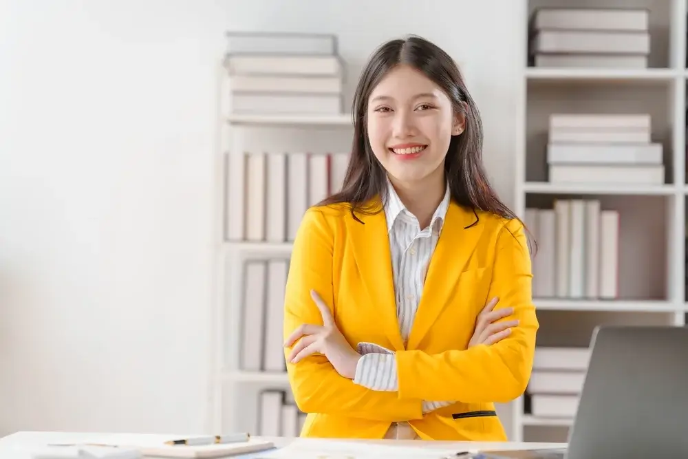 A confident business analyst in a yellow blazer standing in an office, specializing in market analysis and data-driven business insights for growth.