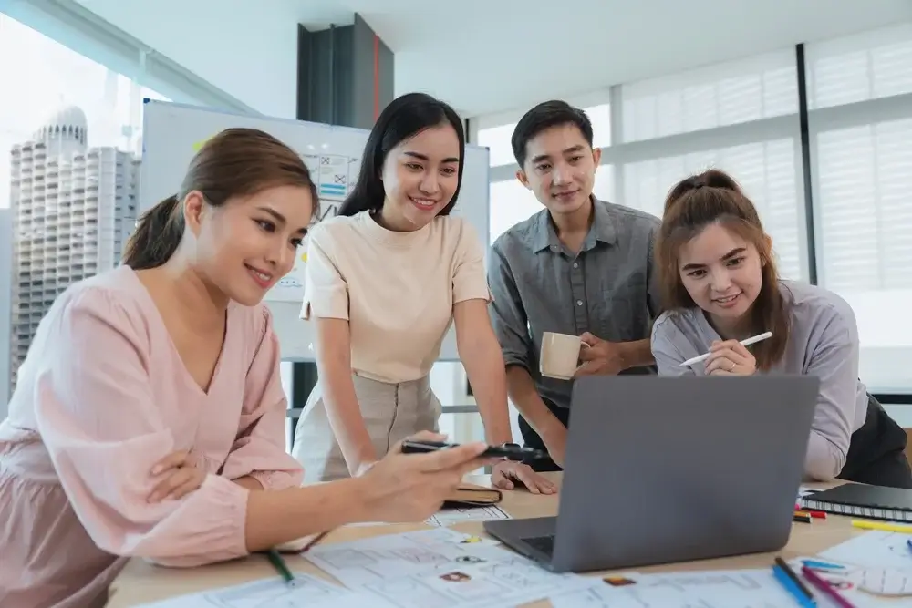 A diverse group of professionals collaborating on a laptop in a modern office, brainstorming ideas for Small Business Innovation Research Assistance.